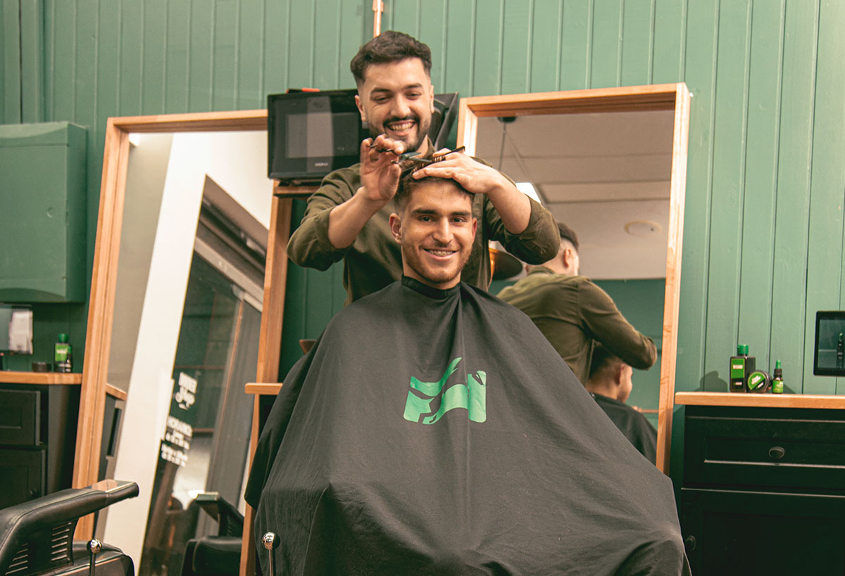 Barbero Verouomo cortando el pelo con tijera a un cliente